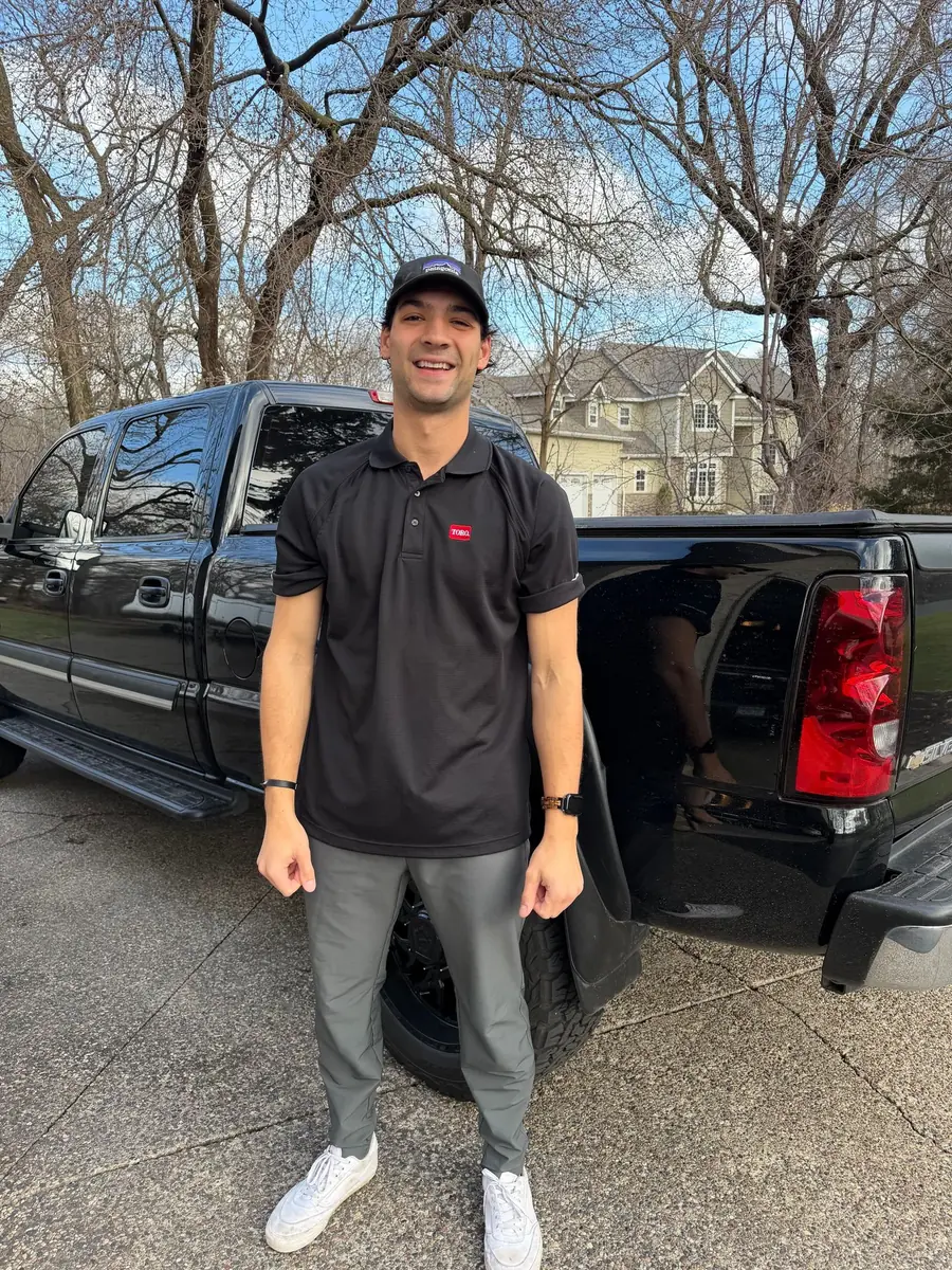 A Heads Up crew member in a Toro polo by the work truck on a suburban driveway