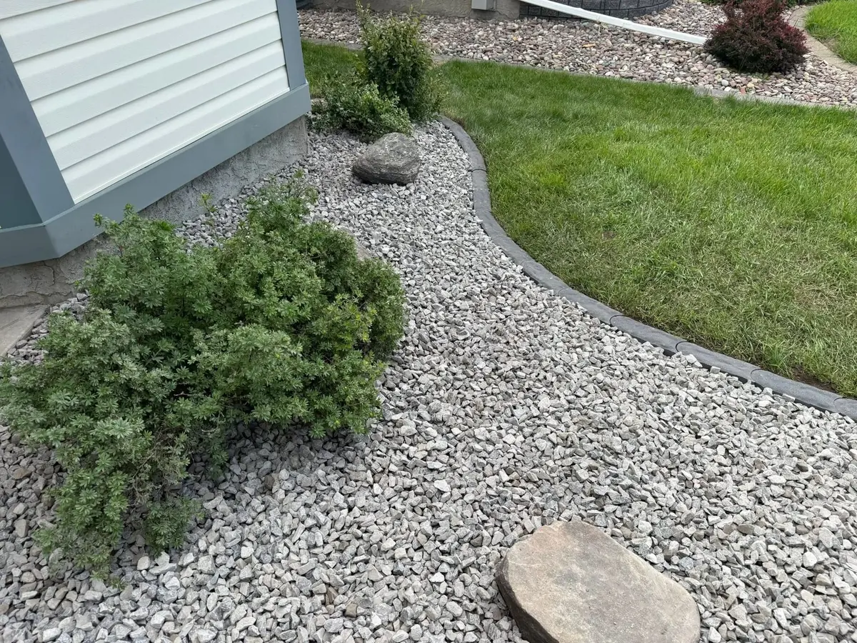 A river-rock bed with low shrubs and a single stepping stone at the lawn edge